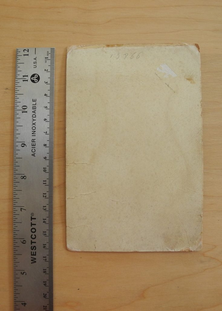 Overhead image of the back of a beige cabinet card. A metallic ruler is placed along the left side of the card.